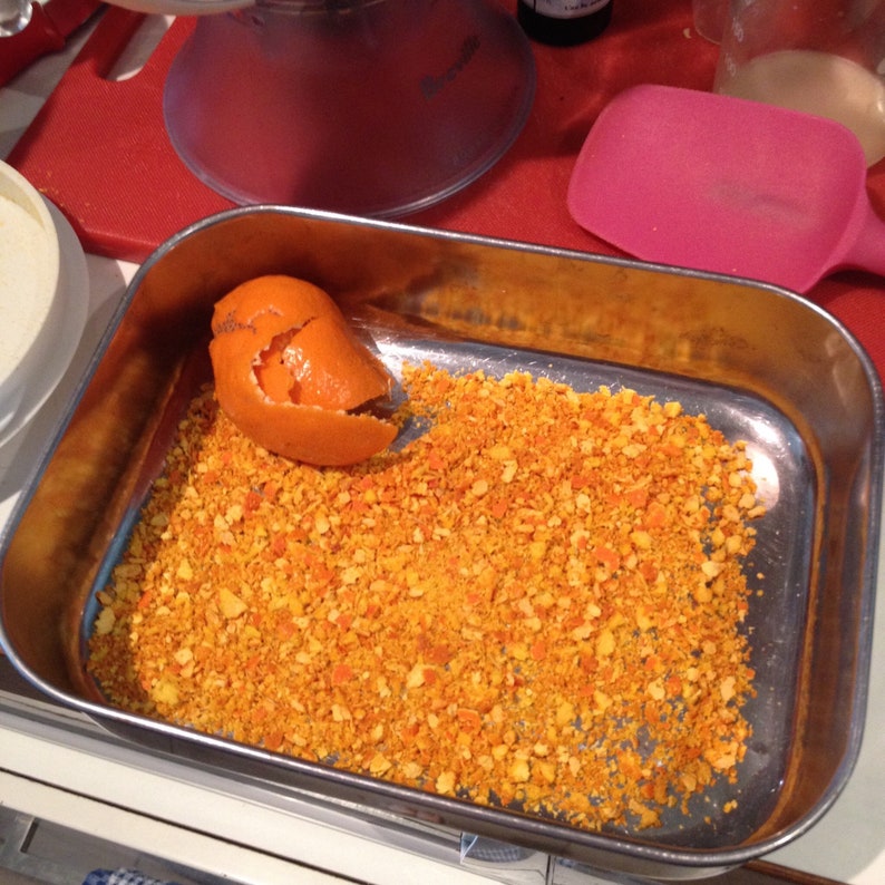 May include: A silver baking dish filled with orange zest, a bright orange peel sits on top of the zest.