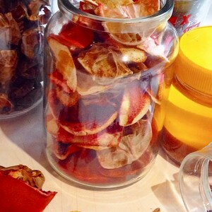 May include: Two glass jars filled with dried orange peels and spices. The jars are on a white surface with loose spices scattered around them.