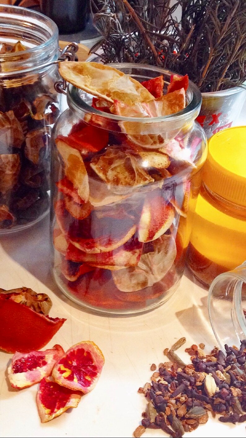 May include: Two glass jars filled with dried orange peels and spices. The jars are on a white surface with loose spices scattered around them.