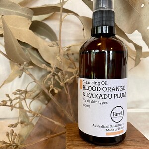 May include: A brown glass bottle with a black pump top and a white label. The label reads "Cleansing Oil Blood Orange & Kakadu Plum For all skin types. 100ml Parva Australian I Small Batch Made by Hand".