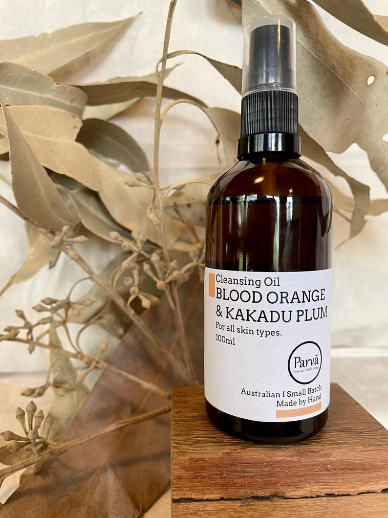 May include: A brown glass bottle with a black pump top and a white label. The label reads "Cleansing Oil Blood Orange & Kakadu Plum For all skin types. 100ml Parva Australian I Small Batch Made by Hand".