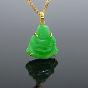 May include: A green jade pendant of a smiling Buddha figure, carved in a sitting pose, with gold accents around the edges. The pendant is attached to a gold chain.