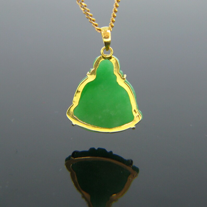 May include: A gold pendant necklace featuring a green jade Buddha figurine. The pendant is detailed with gold trim and the Buddha is sitting in a meditative pose.