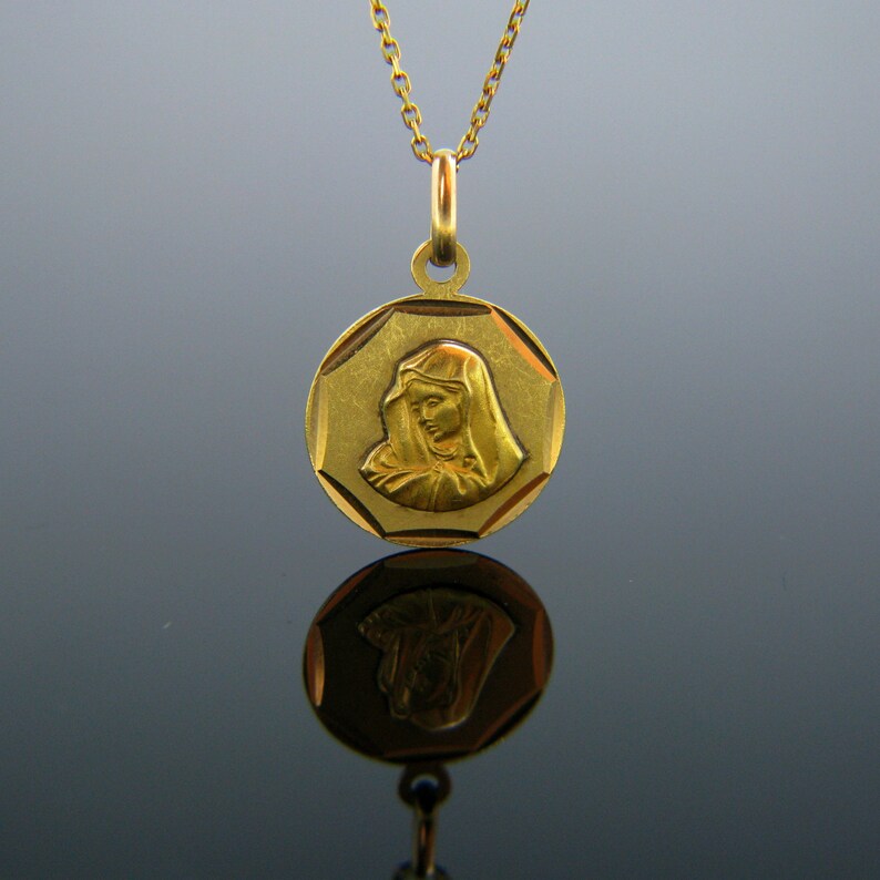 Puede incluir: Un collar de oro con un colgante redondo de forma octogonal que presenta una imagen en relieve de la Virgen Mar&iacute;a. El colgante est&aacute; suspendido de una delicada cadena de oro.