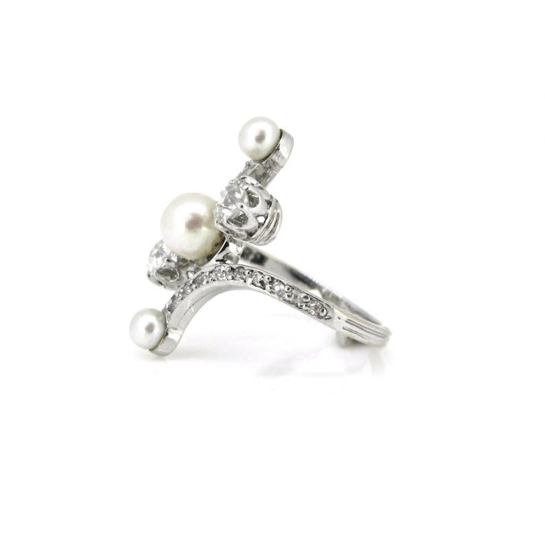 May include: A silver ring with a curved design and three white pearls. The ring is set with small clear stones.