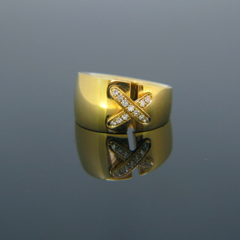 May include: A gold ring with a diamond-encrusted X design. The ring is polished and has a smooth, rounded surface.
