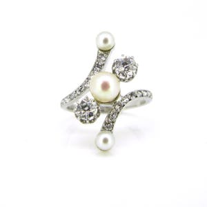 May include: A silver ring with a pearl and three small diamonds. The ring has a curved design.