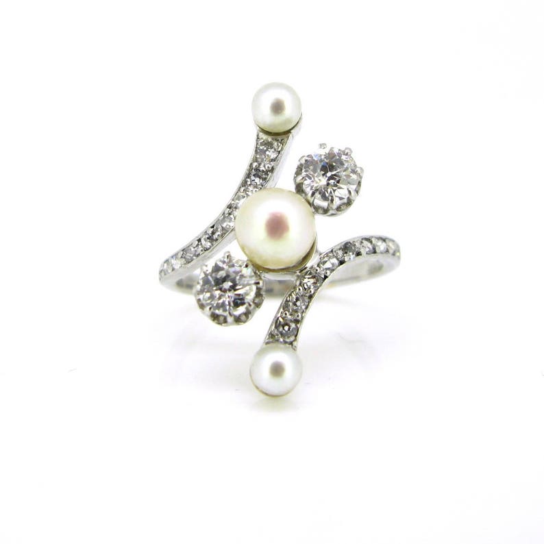 May include: A silver ring with a pearl and three small diamonds. The ring has a curved design.