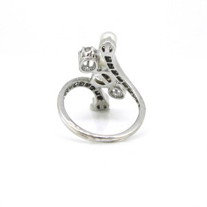 May include: A silver ring with a pearl and clear stones set in a delicate, swirling design.