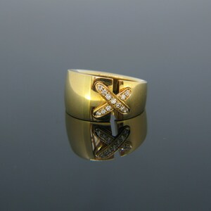 May include: A gold ring with a diamond-encrusted X design. The ring is wide and has a polished finish.