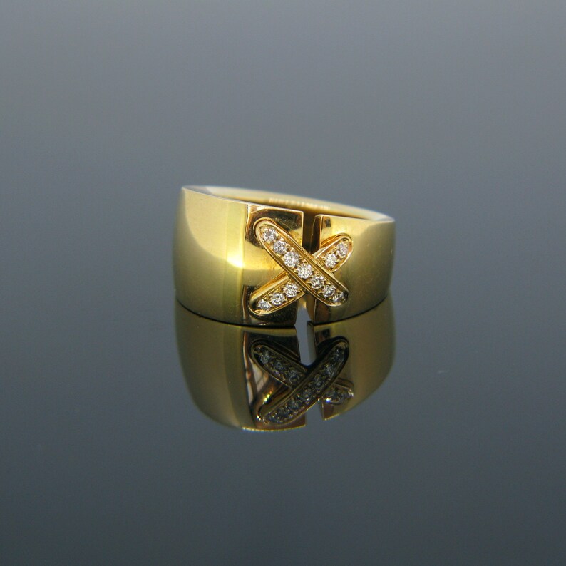 May include: A gold ring with a diamond-encrusted X design. The ring is wide and has a polished finish.