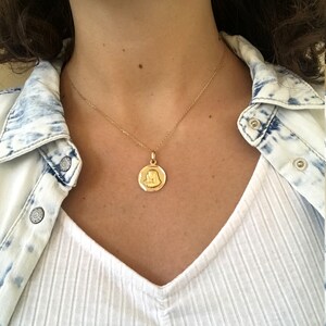 Puede incluir: Un collar de cadena de oro con un colgante redondo que presenta una imagen en relieve de la cara de una mujer.