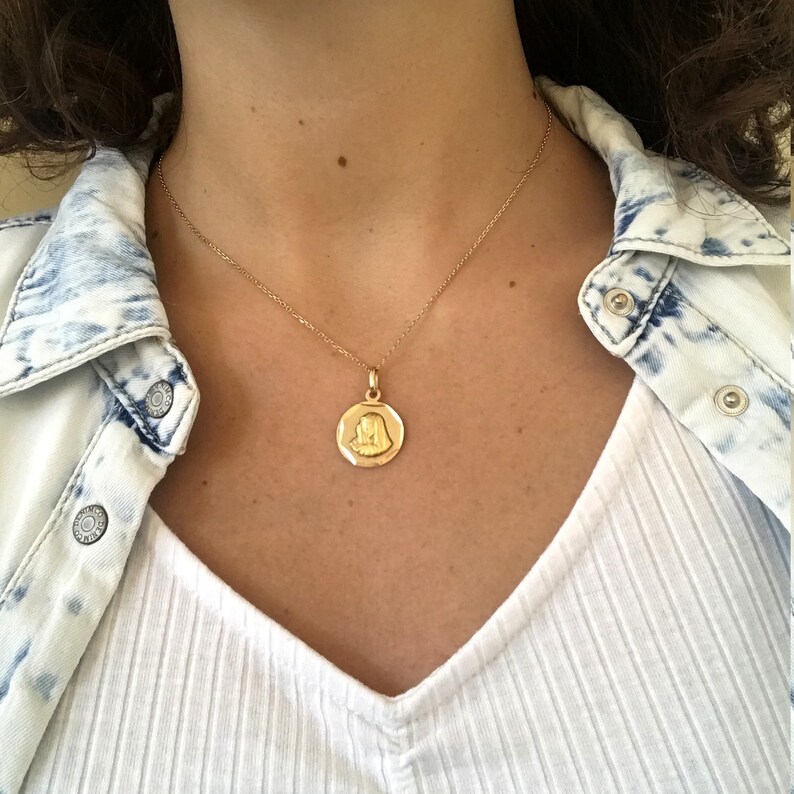 Puede incluir: Un collar de cadena de oro con un colgante redondo que presenta una imagen en relieve de la cara de una mujer.