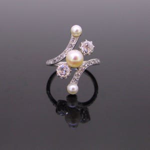 May include: A silver ring with a curved design featuring a cluster of pearls and diamonds. The ring has a delicate and intricate design.