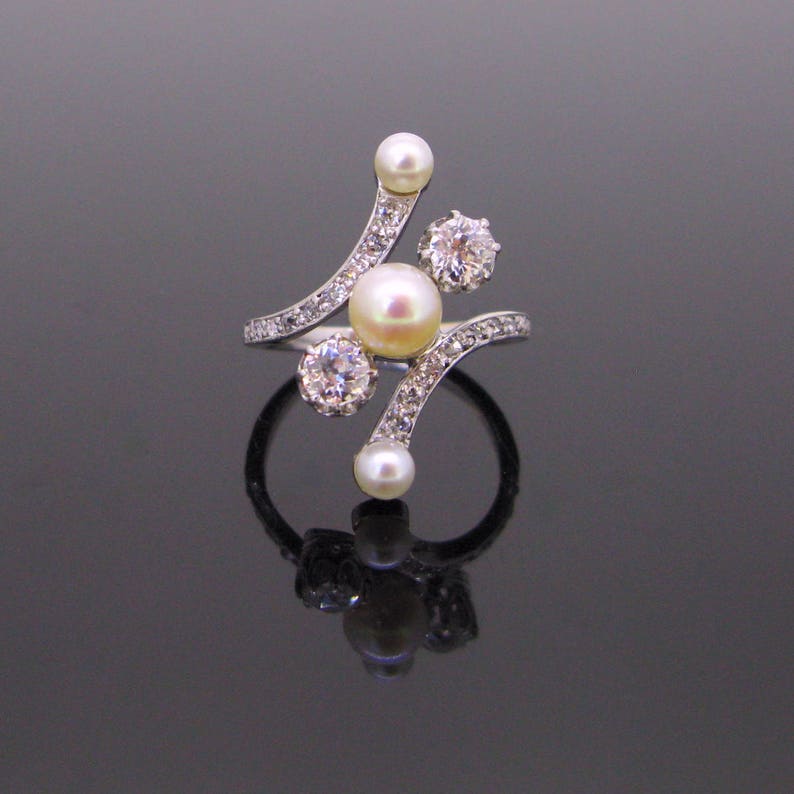 May include: A silver ring with a curved design featuring a cluster of pearls and diamonds. The ring has a delicate and intricate design.