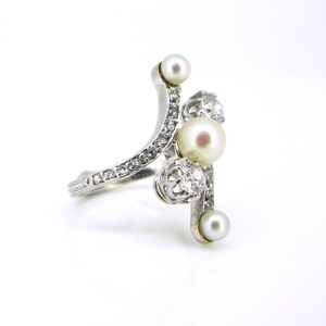 May include: A silver ring with a curved band set with small diamonds and three pearls. The ring has a unique design with the pearls set in a cluster.