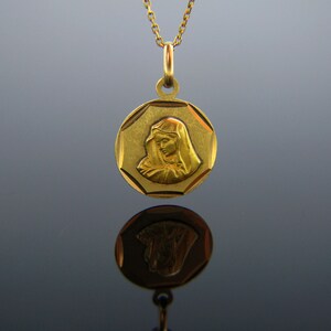 Puede incluir: Un collar de oro con un colgante redondo de forma octogonal que presenta una imagen en relieve de la Virgen Mar&iacute;a. El colgante tiene una superficie texturizada y una cadena de oro.