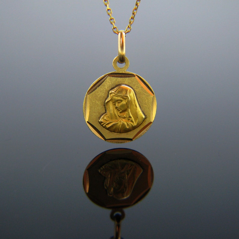 Puede incluir: Un collar de oro con un colgante redondo de forma octogonal que presenta una imagen en relieve de la Virgen Mar&iacute;a. El colgante tiene una superficie texturizada y una cadena de oro.