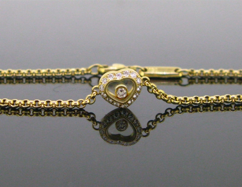 May include: A gold chain bracelet with a heart-shaped pendant featuring a floating diamond. The pendant is set with smaller diamonds around the edge.