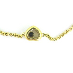 May include: A gold chain bracelet with a heart-shaped pendant. The pendant has a clear window that reveals a small, round, black object inside.