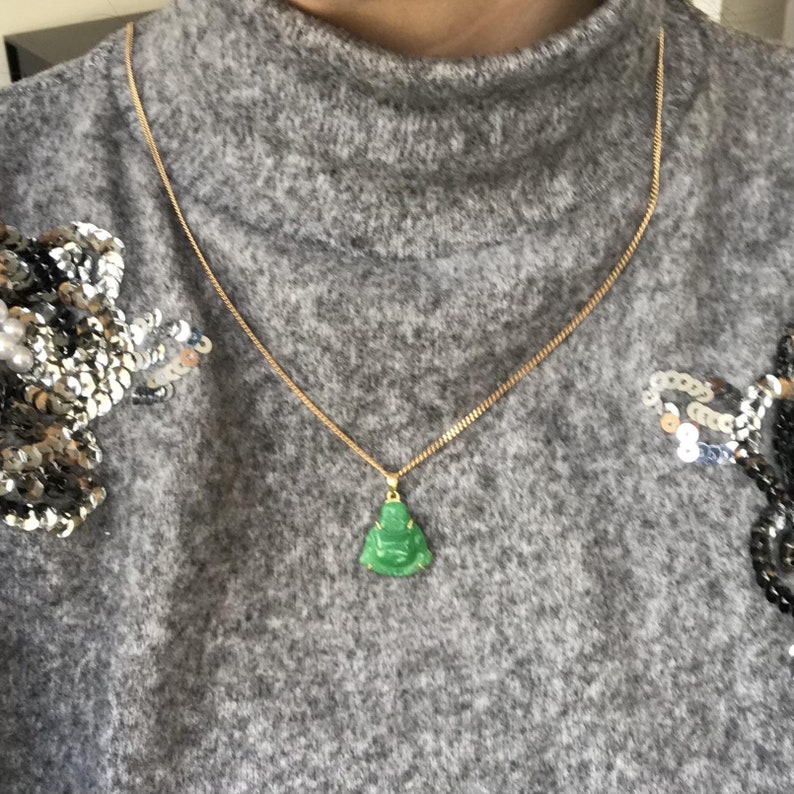 May include: A gold chain necklace with a green jade Buddha pendant.