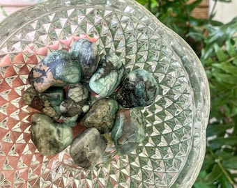 May include: A collection of tumbled emerald green stones in a clear glass bowl with a diamond pattern. The stones are various sizes and shapes.