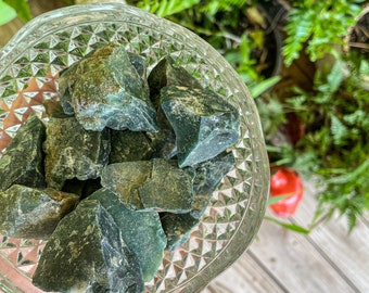 Puede incluir: Un cuenco de vidrio transparente lleno de piedras pulidas verdes y marrones. El cuenco está sobre una superficie de madera.