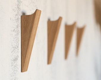 Op de afbeelding: Vier houten wandhaken in een rij, elk in de vorm van een driehoek met afgeronde randen. De haken zijn gemonteerd op een witte muur.