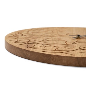 May include: A round wooden clock with a tree branch design carved into the face. The clock has black hands and a silver centre.