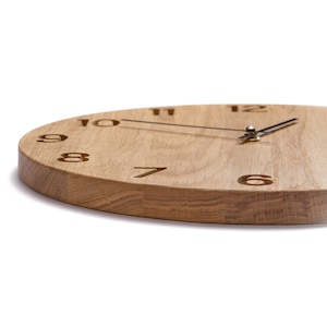 Può includere: Un orologio in legno con numeri romani e lancette nere. L'orologio è in legno marrone chiaro e ha un design semplice.