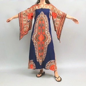 Puede incluir: Un vestido largo azul maxi con un patrón geométrico en naranja, rojo y blanco. El vestido tiene mangas anchas acampanadas y un escote en V.