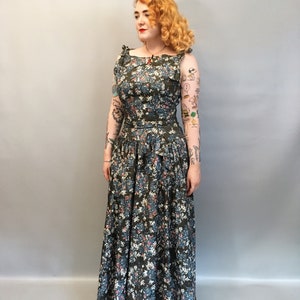 Puede incluir: Una mujer lleva un vestido largo de estampado floral verde con un corpi&ntilde;o ajustado y una falda completa. El vestido tiene un escote cuadrado y tirantes finos. La mujer tiene el pelo rojo y lleva un collar rojo.