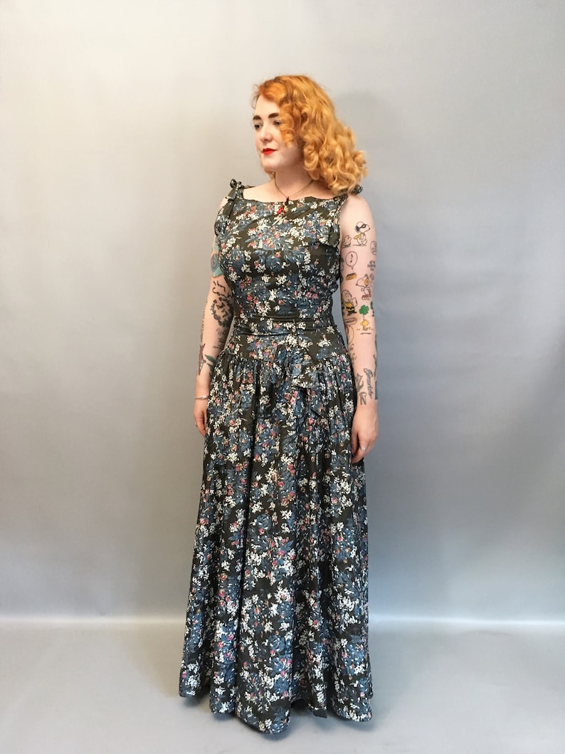 Puede incluir: Una mujer lleva un vestido largo de estampado floral verde con un corpi&ntilde;o ajustado y una falda completa. El vestido tiene un escote cuadrado y tirantes finos. La mujer tiene el pelo rojo y lleva un collar rojo.