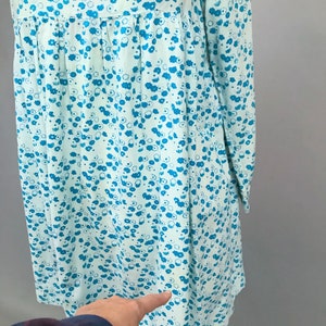 May include: A light blue dress with a white background and a blue floral pattern. The dress has long sleeves and a gathered waist.