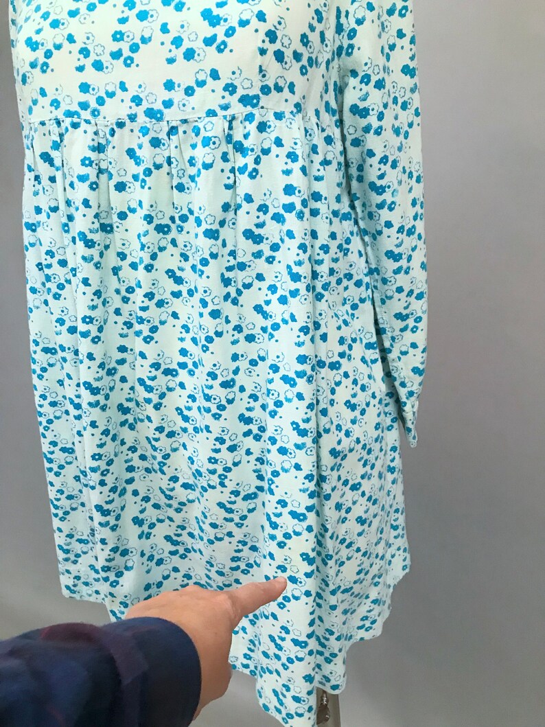May include: A light blue dress with a white background and a blue floral pattern. The dress has long sleeves and a gathered waist.