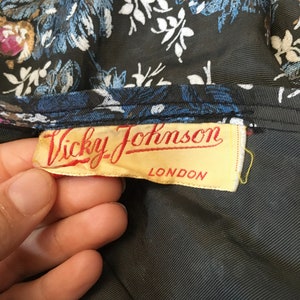 Puede incluir: Una tela negra con un patr&oacute;n floral y una etiqueta amarilla que dice "Vicky Johnson LONDON".