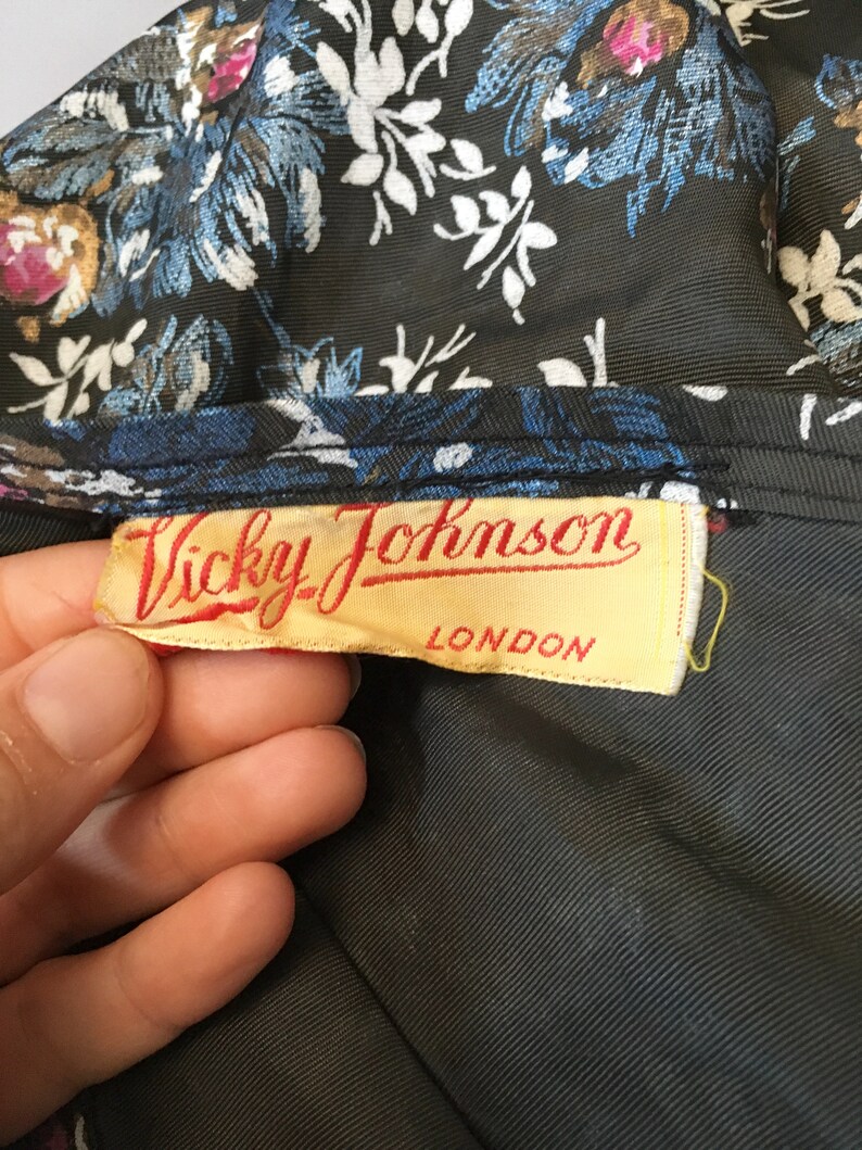 Puede incluir: Una tela negra con un patr&oacute;n floral y una etiqueta amarilla que dice "Vicky Johnson LONDON".