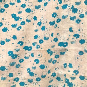 May include: White fabric with a blue floral pattern. The fabric has a slightly textured surface.