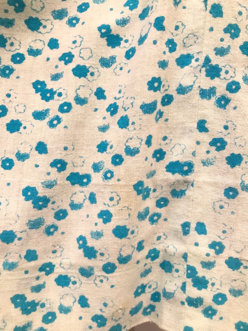 May include: White fabric with a blue floral pattern. The fabric has a slightly textured surface.