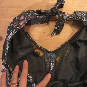 Puede incluir: Un vestido floral azul oscuro con un lazo en el cuello. El vestido tiene una tela transparente y est&aacute; manchado con marcas marrones.