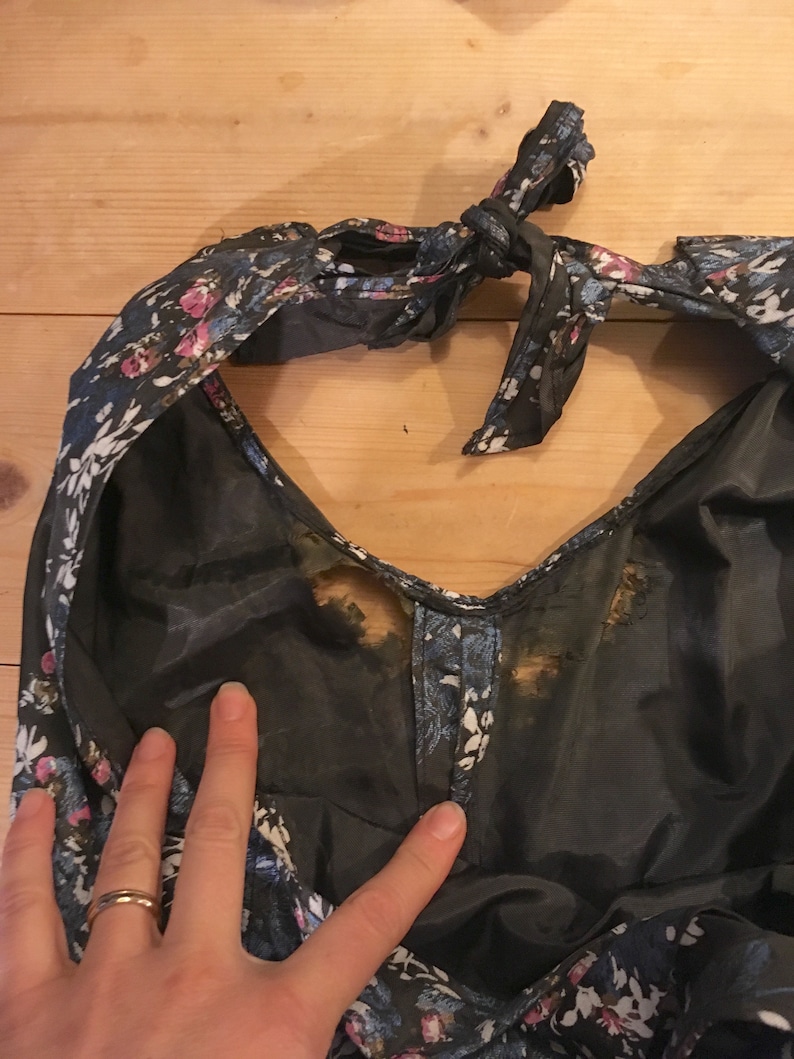 Puede incluir: Un vestido floral azul oscuro con un lazo en el cuello. El vestido tiene una tela transparente y est&aacute; manchado con marcas marrones.