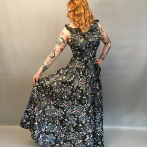 Puede incluir: Un vestido largo de estampado floral con un corpi&ntilde;o ajustado y una falda completa. El vestido es de color verde oscuro con flores azules y rosas.