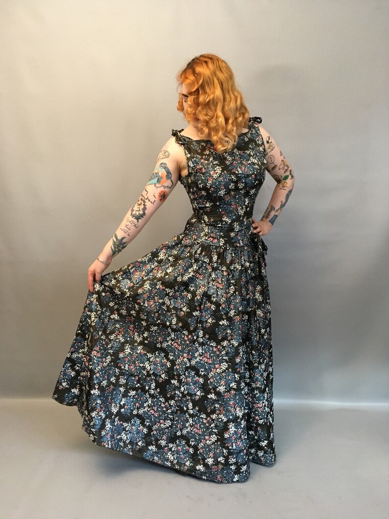 Puede incluir: Un vestido largo de estampado floral con un corpi&ntilde;o ajustado y una falda completa. El vestido es de color verde oscuro con flores azules y rosas.