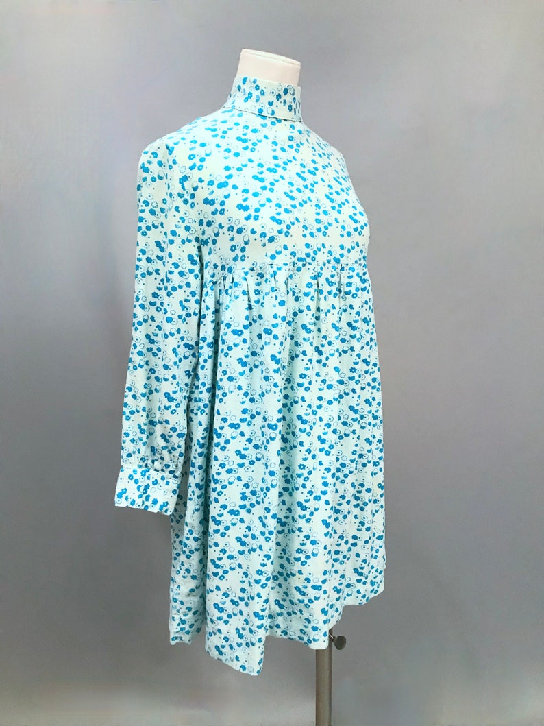 May include: A light blue dress with a high neck and long sleeves. The dress has a small blue floral pattern.