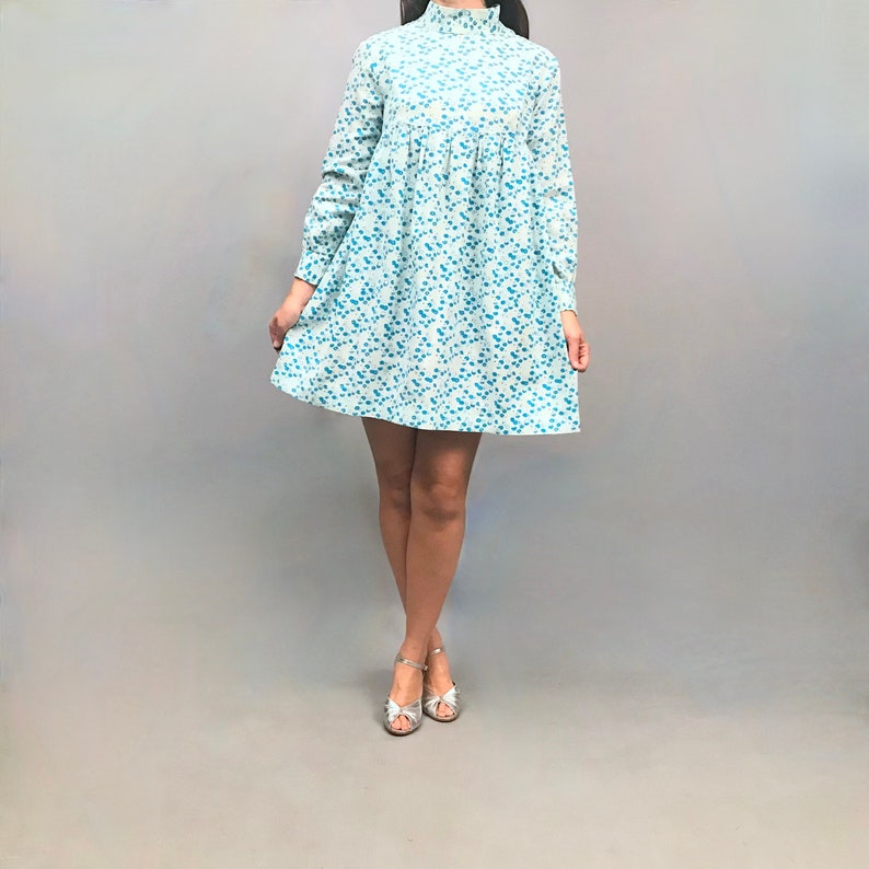 May include: A light blue mini dress with a white floral pattern and a high neck. The dress has long sleeves and a gathered skirt.