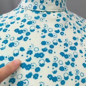 May include: Close-up of a white fabric with a blue floral pattern. The fabric has a textured surface and the flowers are scattered randomly.