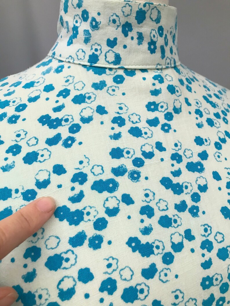May include: Close-up of a white fabric with a blue floral pattern. The fabric has a textured surface and the flowers are scattered randomly.