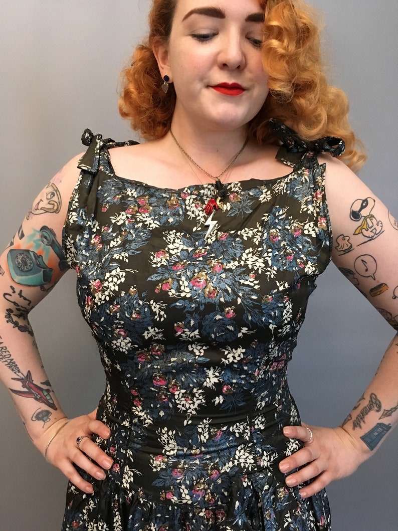Puede incluir: Una mujer lleva un vestido de estampado floral verde con escote cuadrado y tirantes de lazo. El vestido tiene un corpi&ntilde;o ajustado y una falda completa. La mujer tiene el pelo rojo y lleva l&aacute;piz labial rojo.