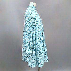 May include: A light blue dress with a white and blue floral pattern. The dress has a high neck and long sleeves. It is fitted at the waist and flows out to a slightly flared skirt.