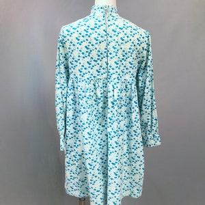 May include: A light blue dress with a white floral pattern. The dress has a high neck and long sleeves. It is made of a soft, comfortable fabric and has a relaxed fit.